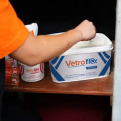 Arm of a person in an orange shirt placing a bag into a white Vetroflex collection container with blue striped graphics.
