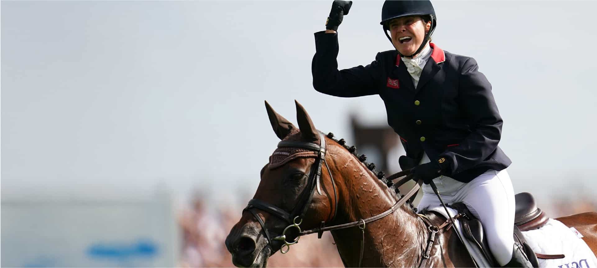 Equestrian rider on a brown horse, wearing a helmet and jacket, raising a gloved fist in victory.